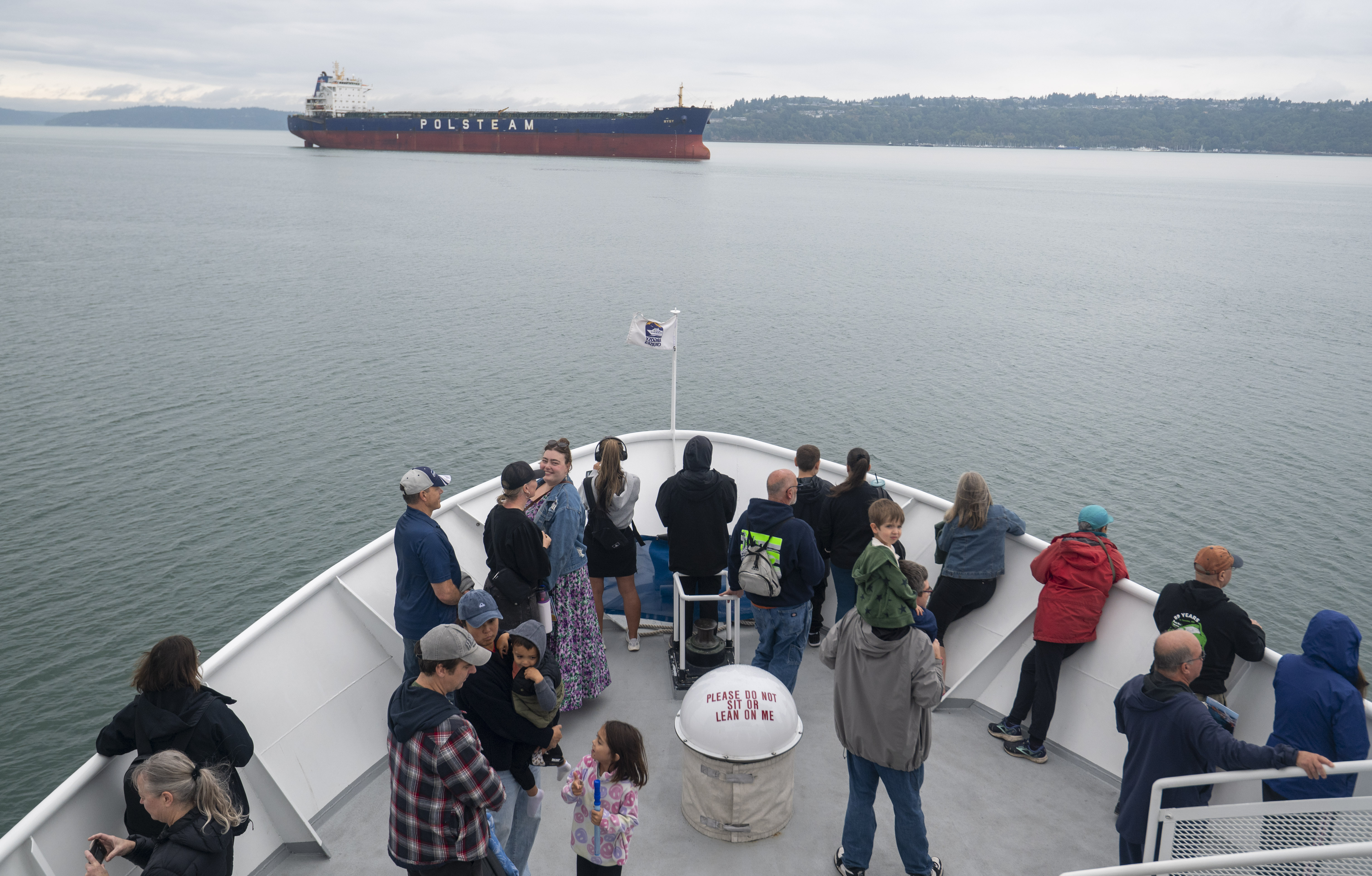A view off the bow of the boat, showing guests and a ship in the distance.