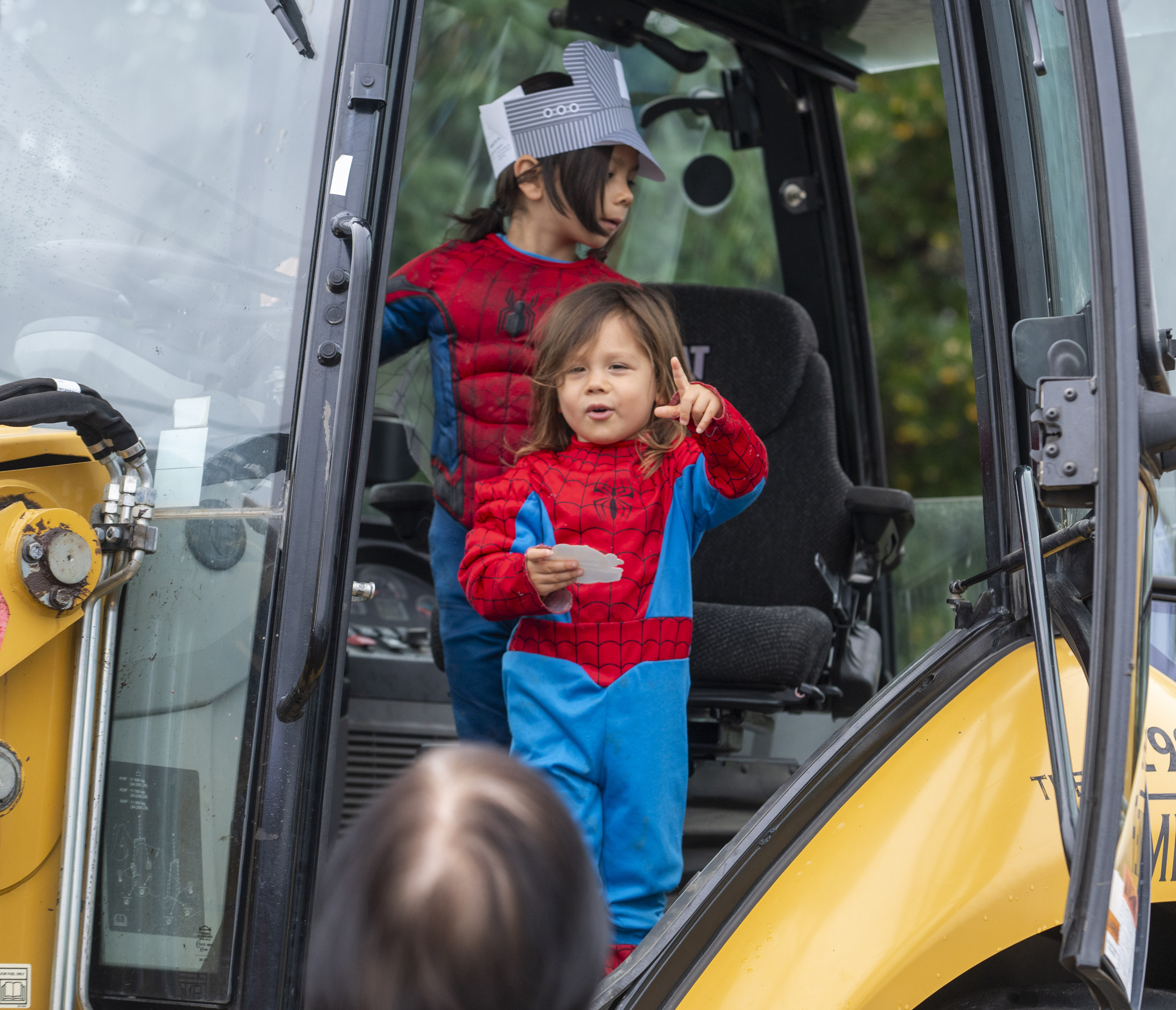 Two children in Spider-man costumes stand in a construction vehicle.